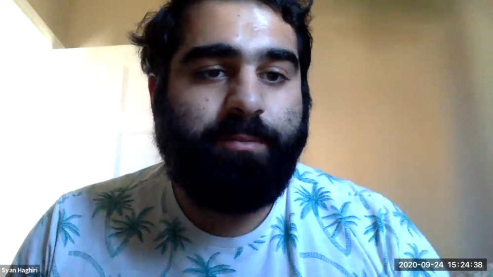 Photo of a person whose name is Syan Haghiri. Syan is looking in the direction of the camera and is wearing a blue shirt with green and beige palm trees on it. Syan has a black beard with black hair. Syan is in the middle of a Zoom meeting for the California Community College Chancellor's Press Conference.