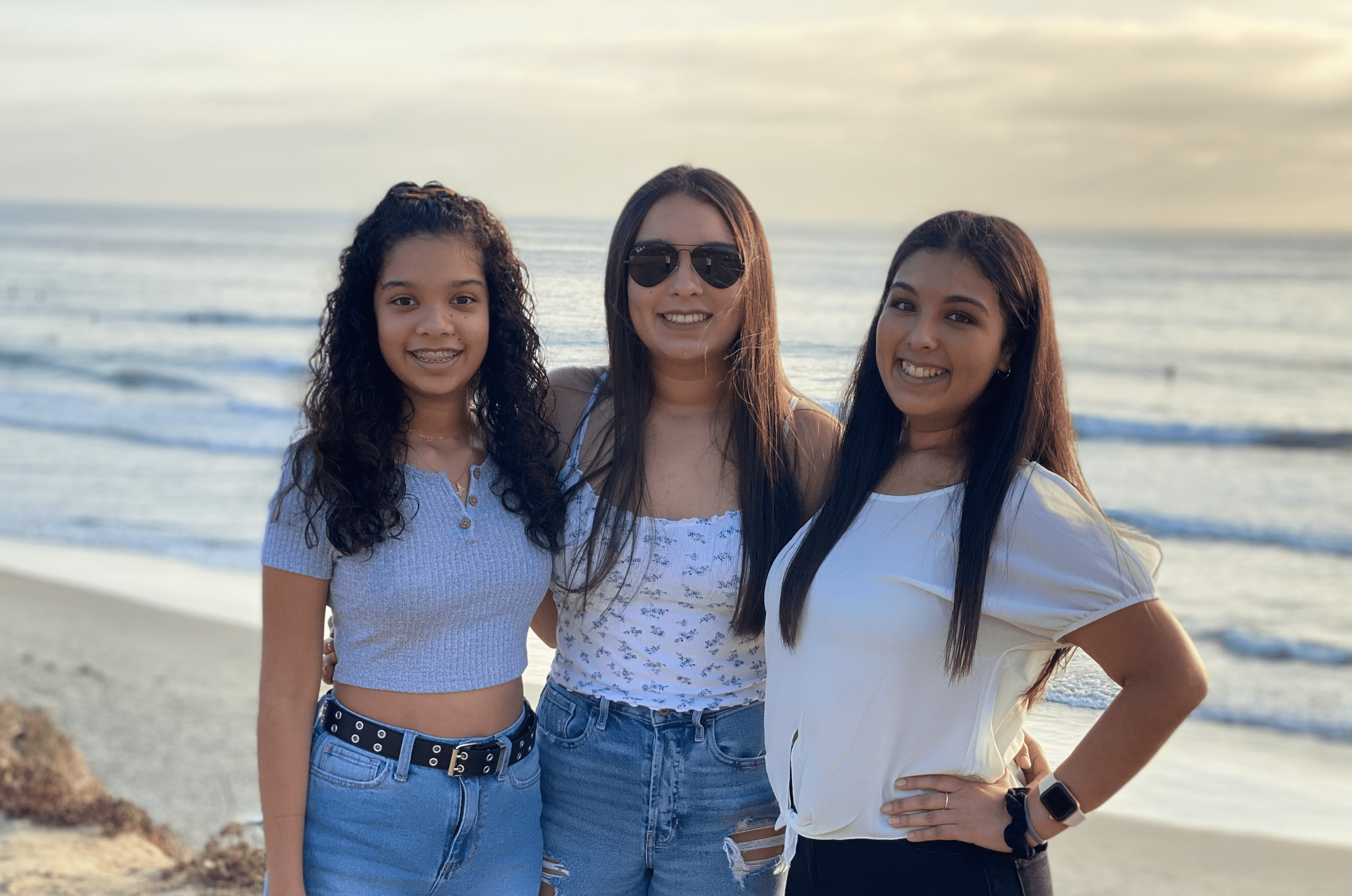 Three girls smiling at the camera on the beach at sunset.